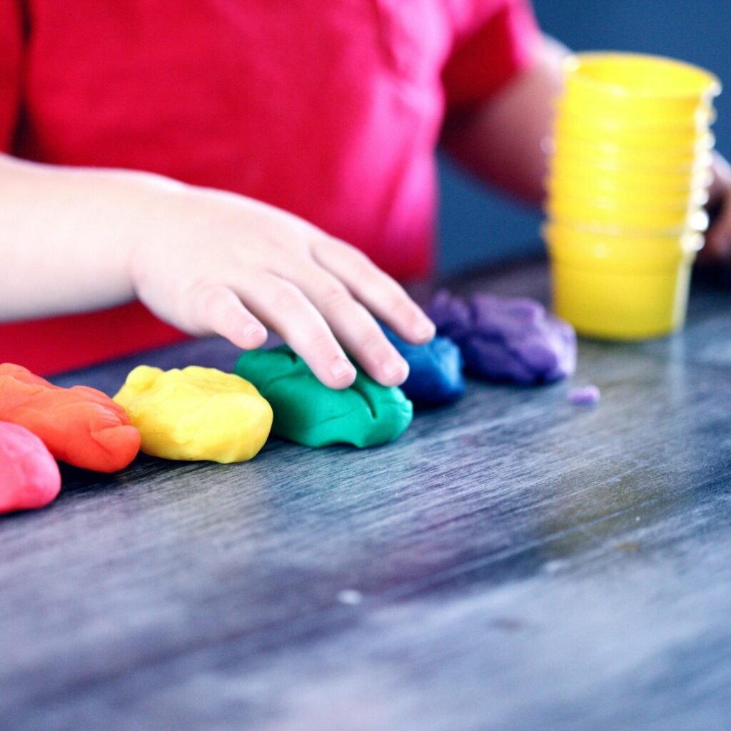 A young child with rainbow-colored modeling clay and stacking cups on a table indoors.