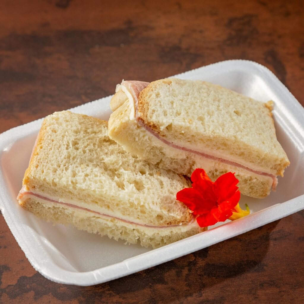 A simple ham sandwich with an edible flower garnish served on a white plate.