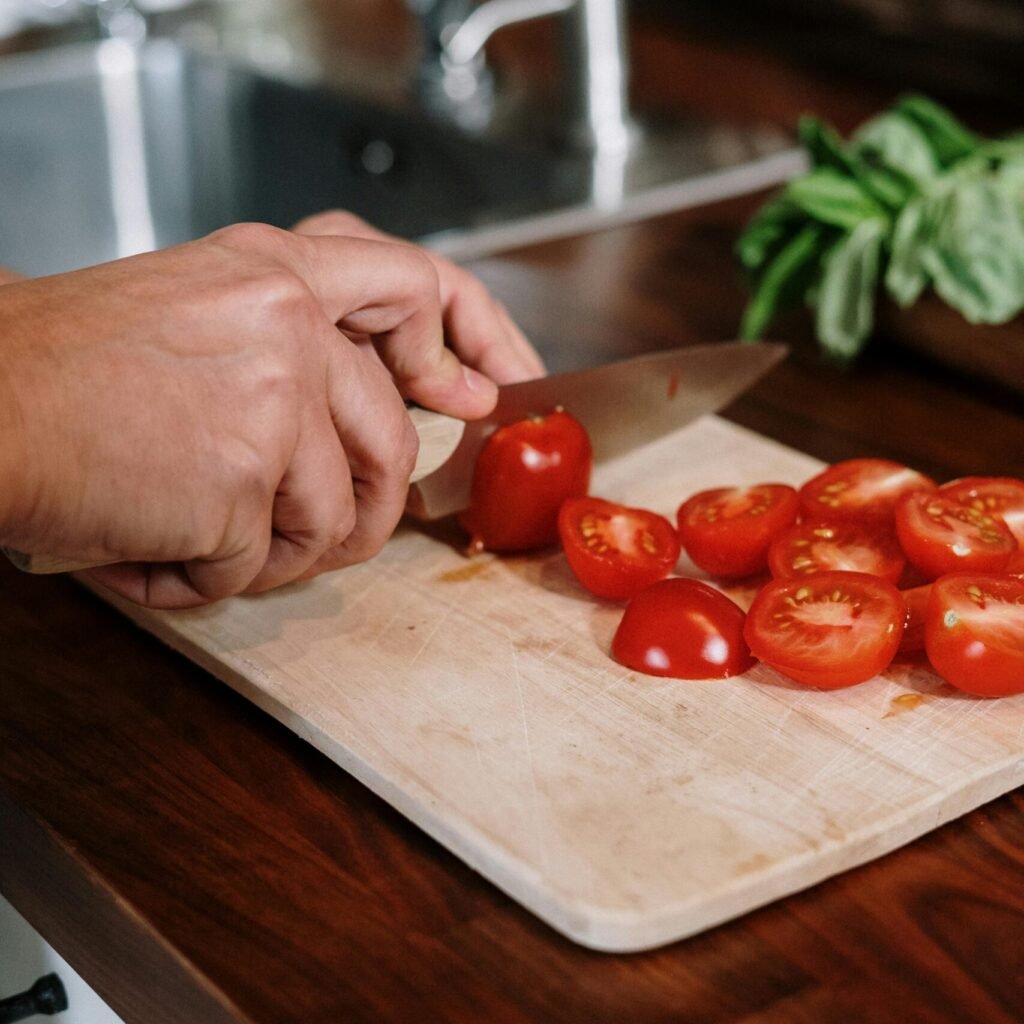 Close-up of hands slicing fresh tomatoes on a wooden cutting board in a cozy kitchen setting.